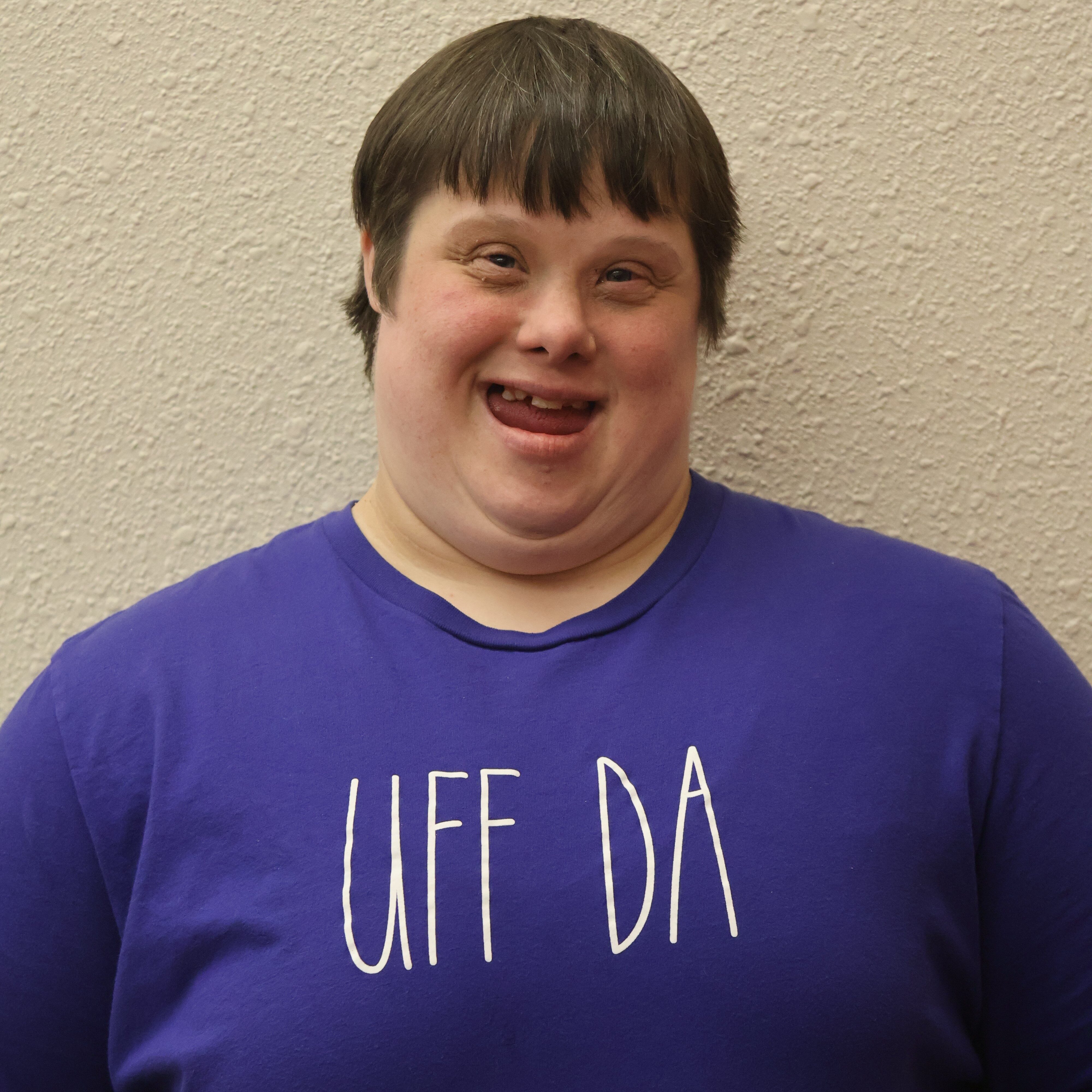 Person smiling while wearing a purple shirt with the phrase 